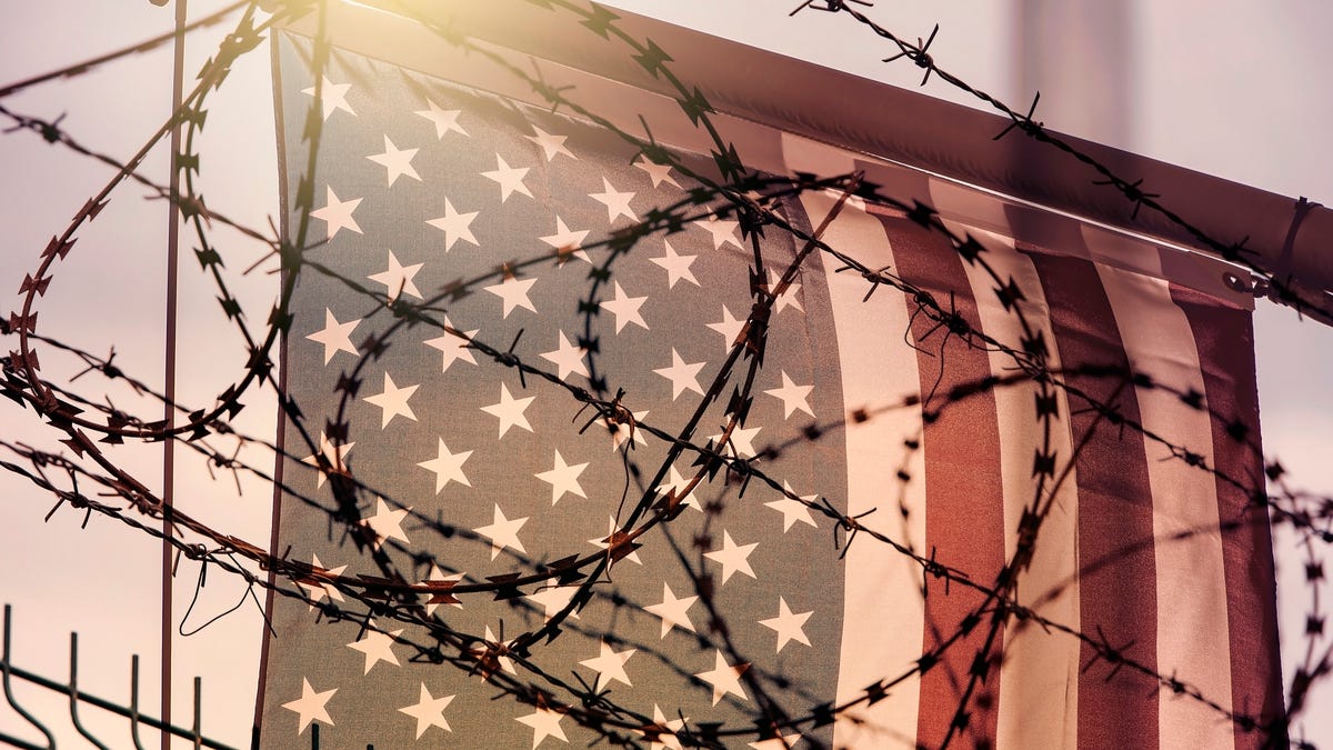 Barbed wire obscures the view of a US flag, pictured at the border.