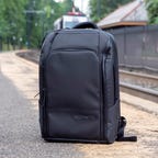Nomatic Travel Backpack sitting on the ground next to railroad tracks