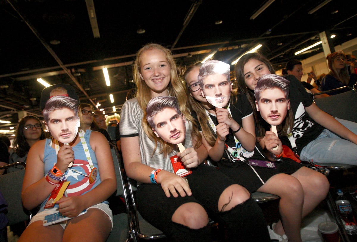Young fans of Joey Graceffa hold masks of his face in front of their own.