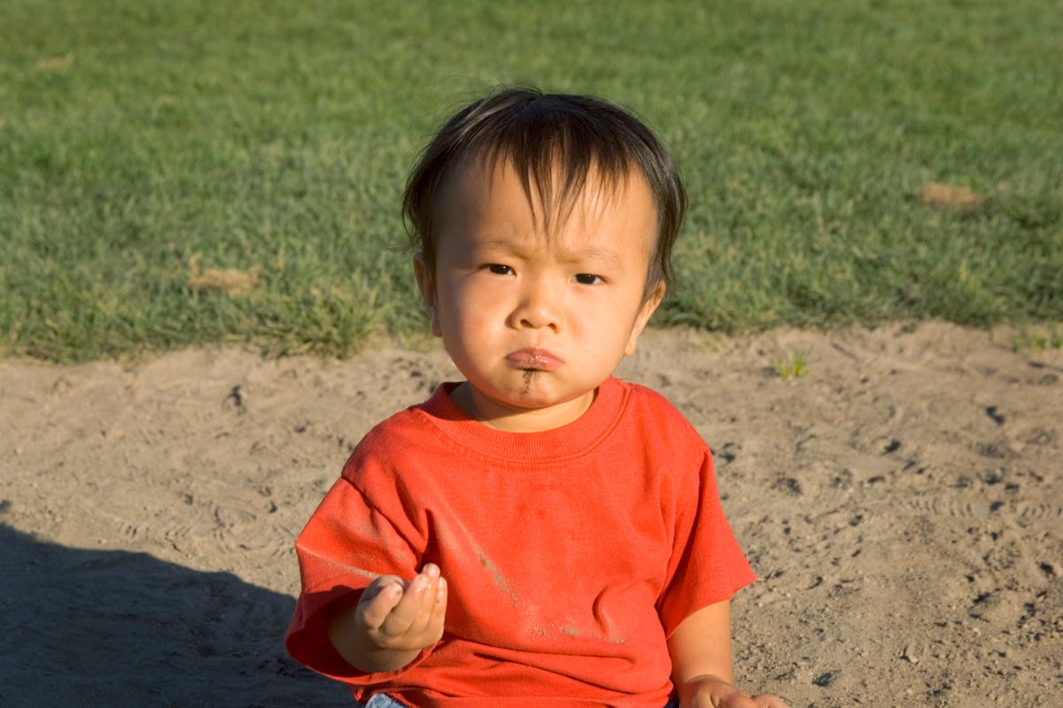 A toddler looking grumpy eating dirt