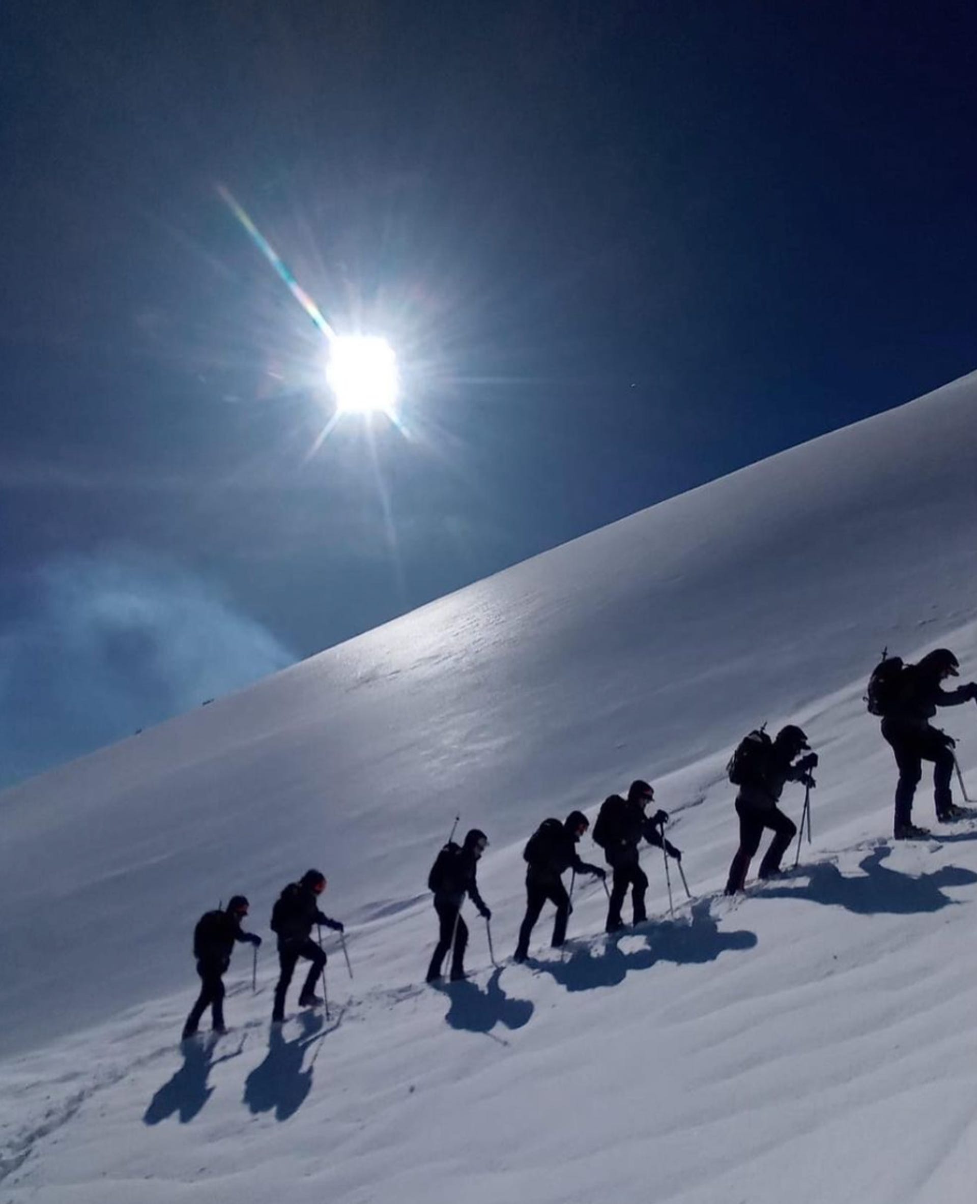 A line of hikers ascend a steep, snowy landscape