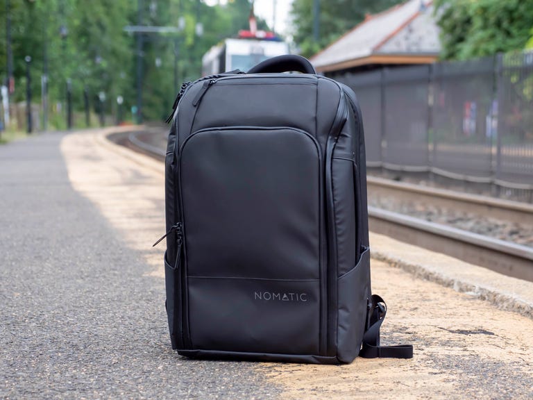 Nomatic Travel Backpack sitting on the ground next to railroad tracks