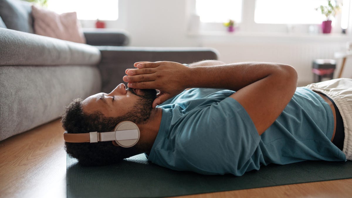 man meditating alone at home while listening to meditation music through wireless headphones