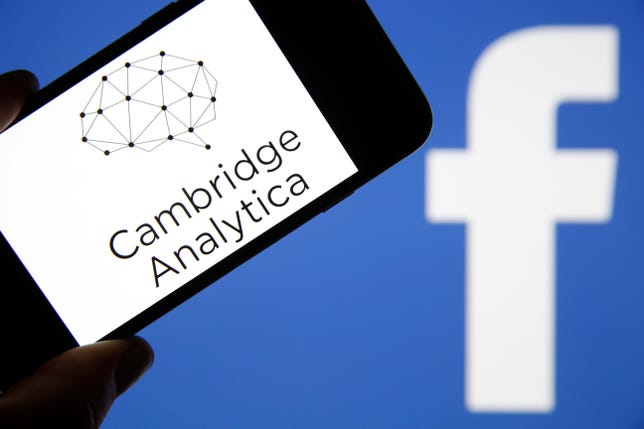 Cambridge Analytica name and logo on a smartphone screen, in front of the Facebook logo.