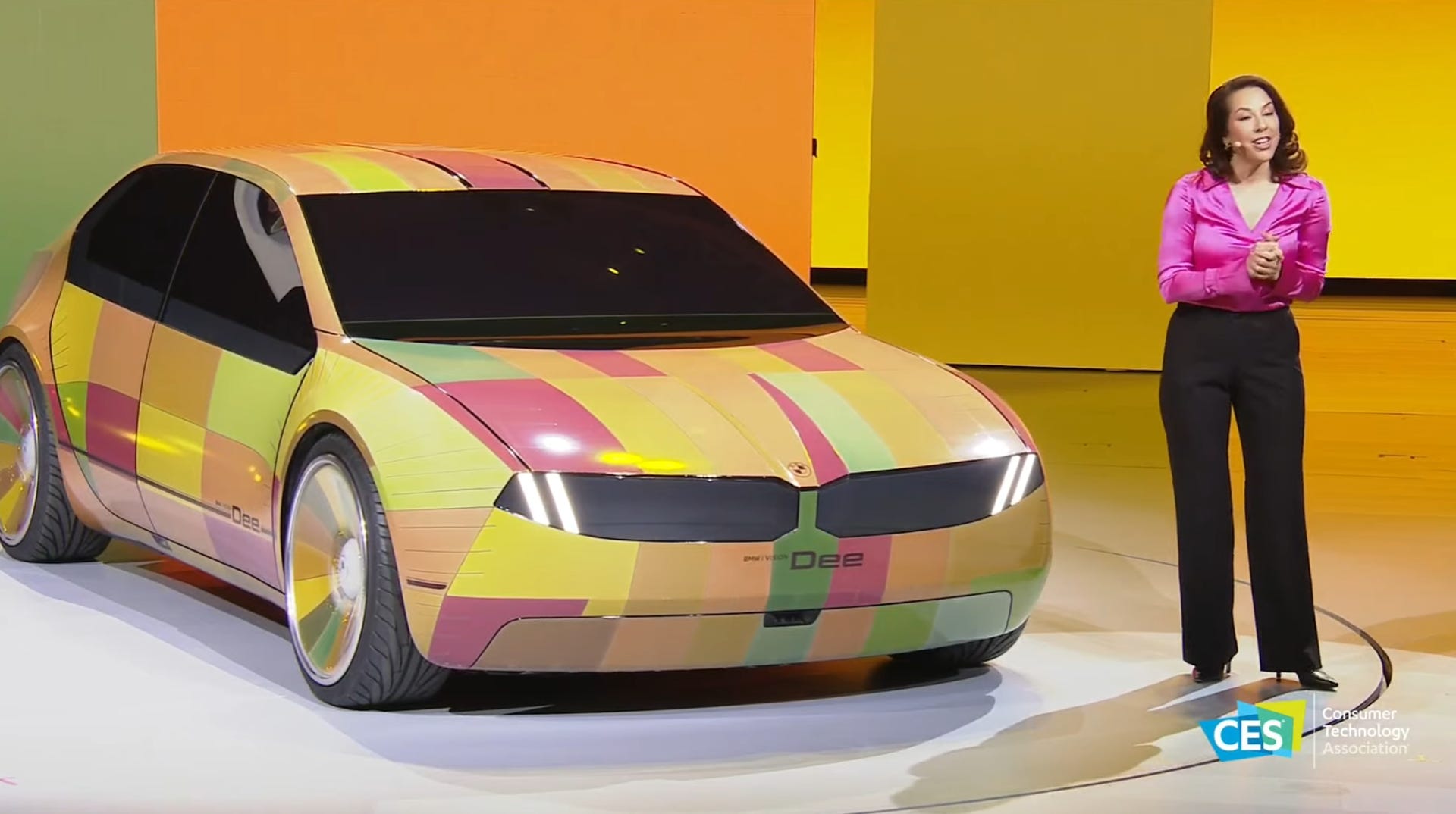 The Dee concept vehicle sits next to a presenter, with the car's outside skin split in geometric zones, all different colors.