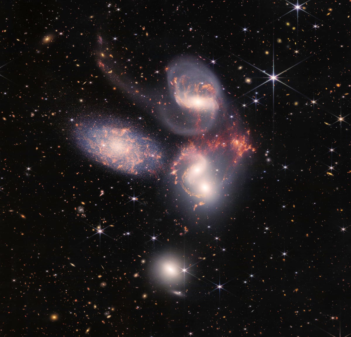 Webb view of five galaxies looking like swirling objects of light against a color-flecked backdrop of space.