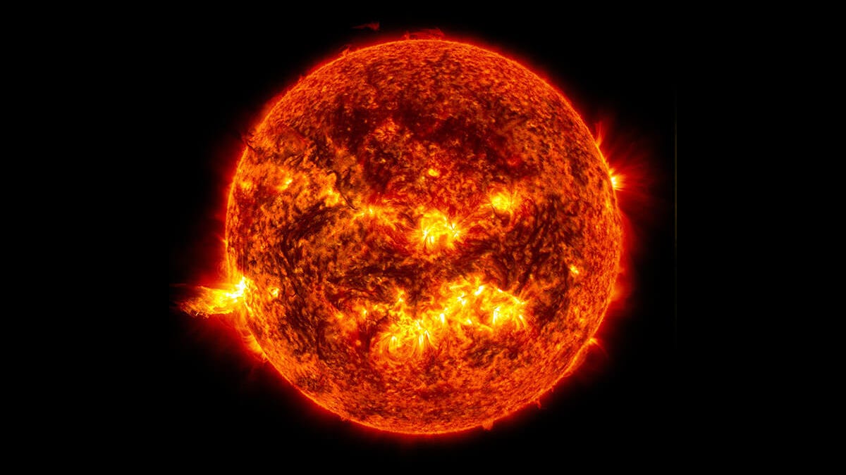 Against the black background of space floats a fiery, bright, red-orange and yellow sun.