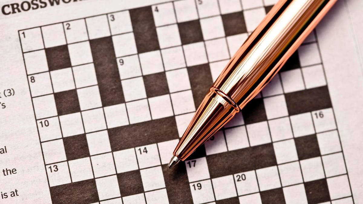 A gold pen on top of an unfinished crossword puzzle