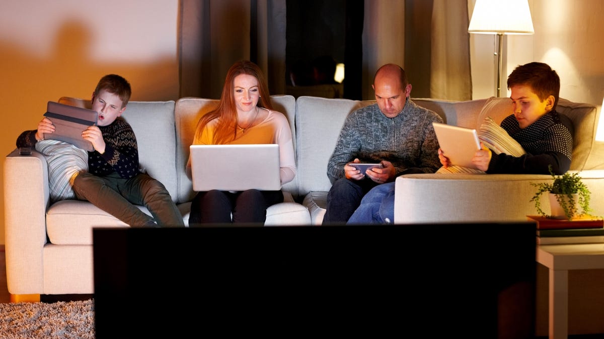 Family of four sitting on couch using digital devices