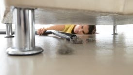 a woman vacuuming up dust from beneath a bed