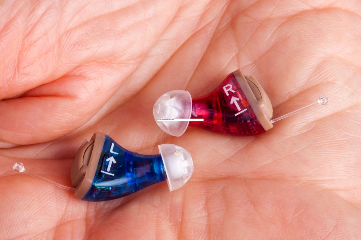 Hand holding two small in-the-ear hearing aids