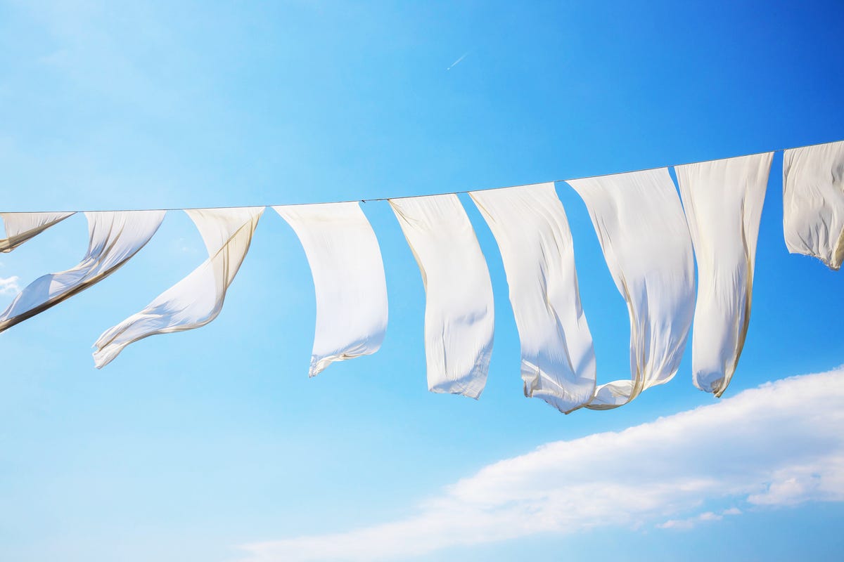 White sheets blow on a clothesline against a blue sky.