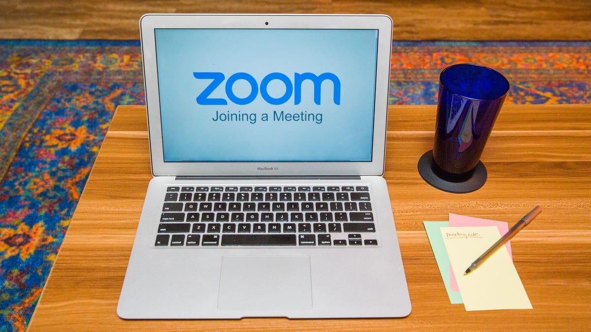 Zoom running on a laptop with a drinking glass and notes next to it on the desk