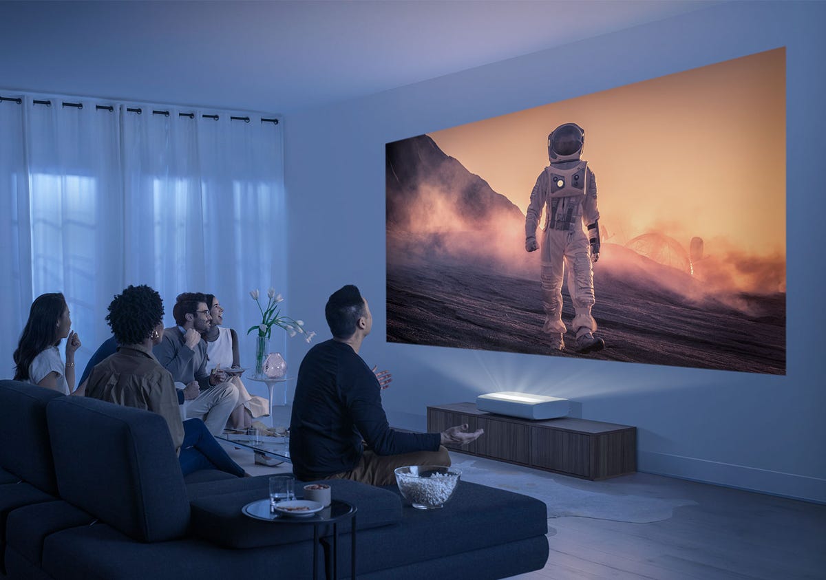 Un salon avec plusieurs personnes regardant une image simulée d'un astronaute sur le mur créée par un projecteur UST.