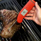 red thermometer sticking into steak on grill