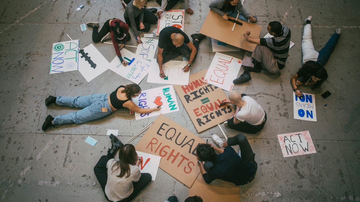 Young people sitting on the ground making protest posters about human rights and equal rights