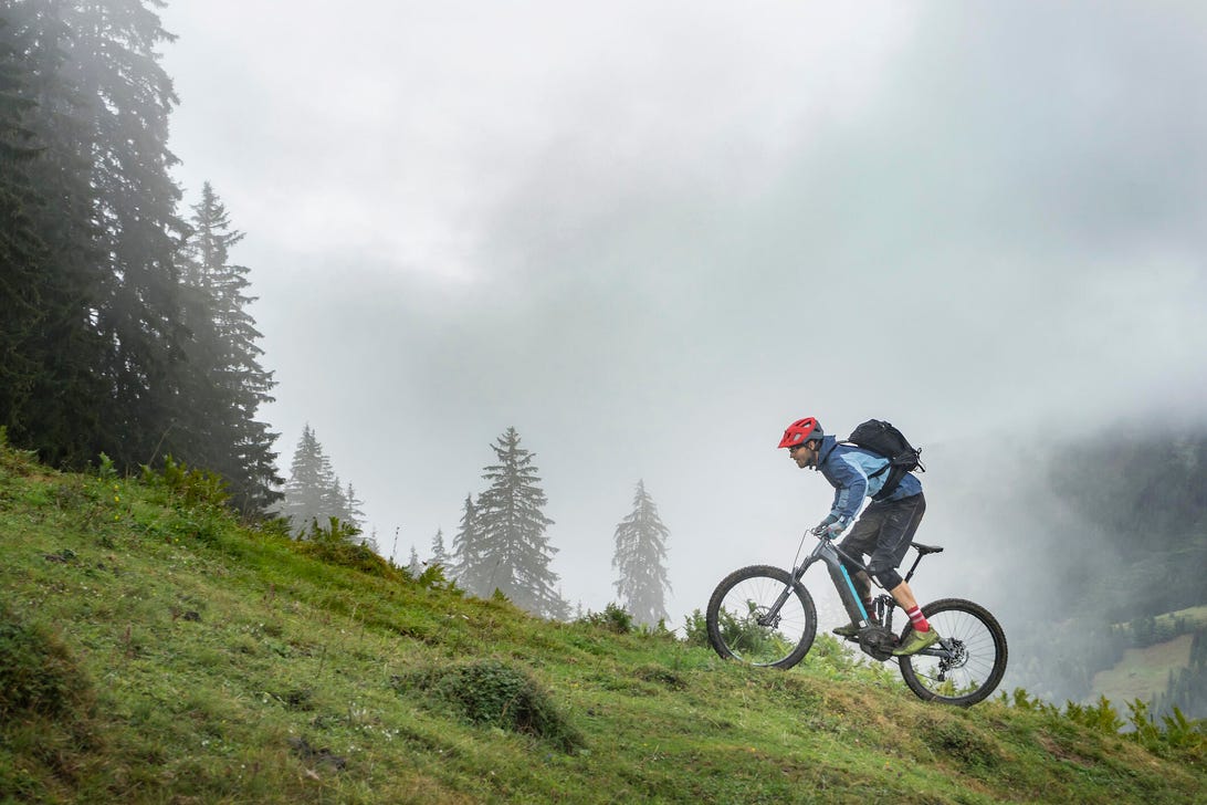 A man rides and e-bike up an incline on a mountain biking trail