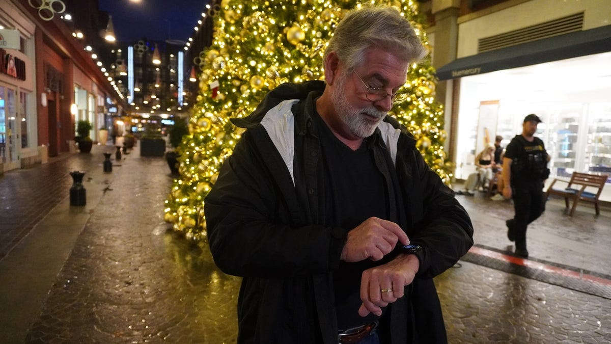A man stands in front of shops checking his Apple Watch