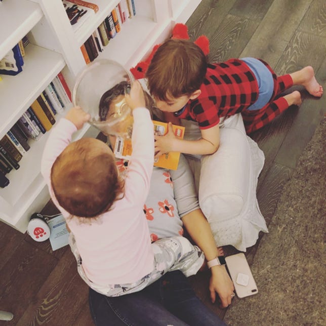 Farnoosh op de vloer met haar twee kinderen die op haar klimmen met speelgoed