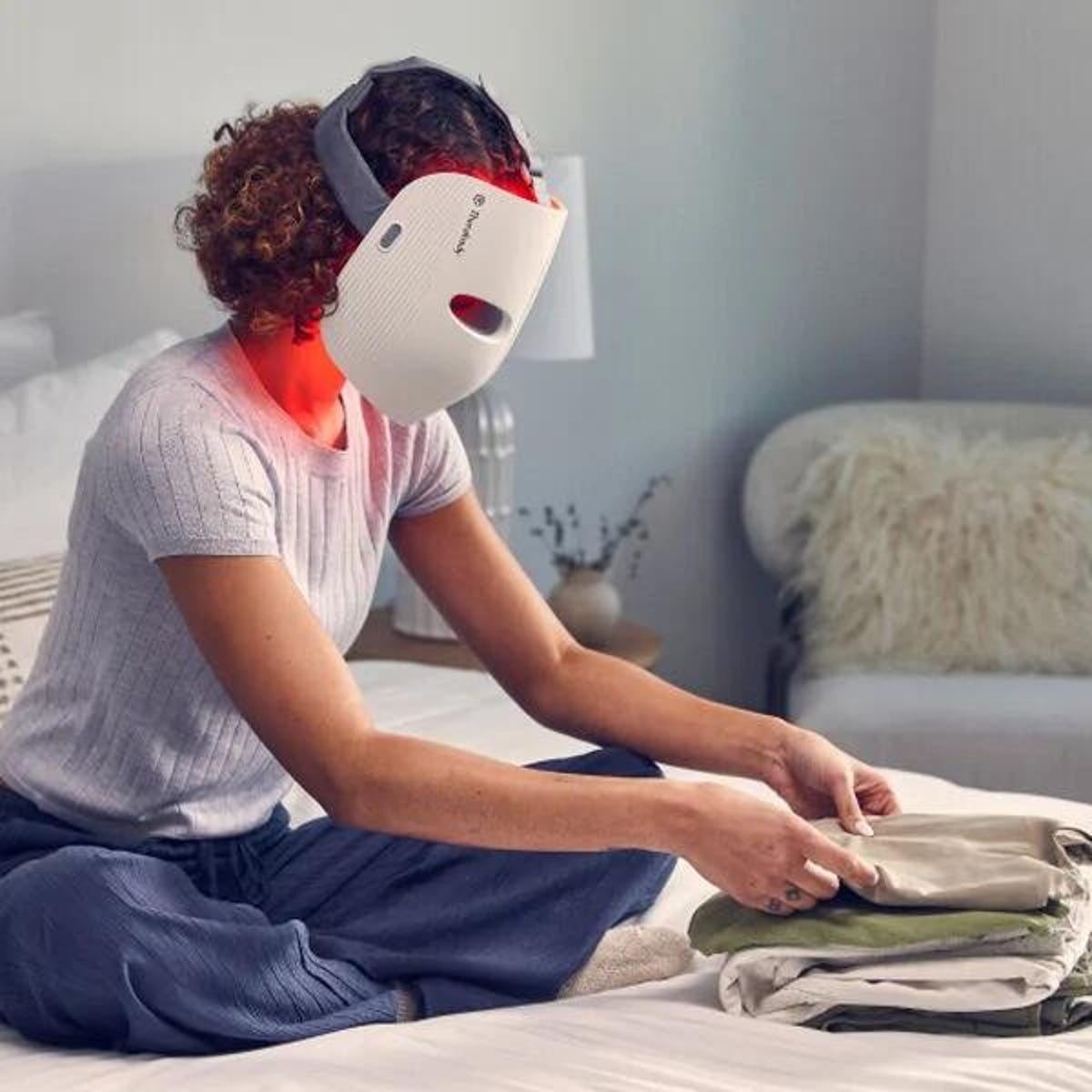 A woman folding clothes in her Therabody LED face mask