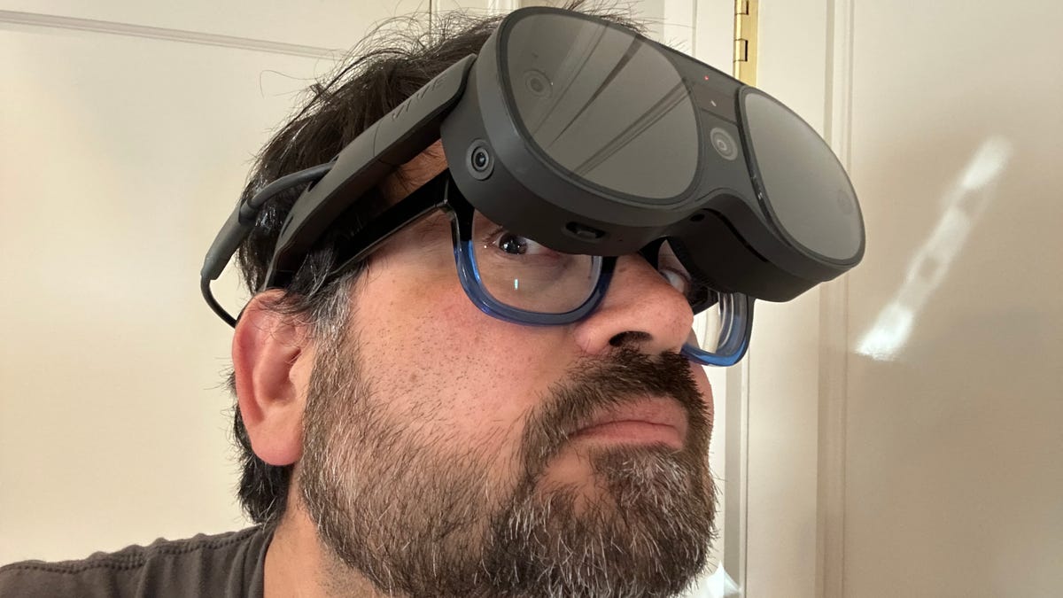 Um homem usando um par de óculos de realidade virtual sobre os próprios óculos, espiando por baixo deles