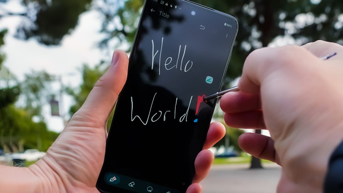 A phone is held up with one hand while the other writes 'Hello World!' on the screen using the stylus.