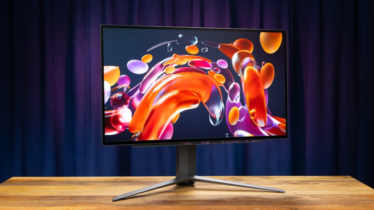 The LG Ultragear OLED 27-inch monitor angled to your right on a wood surface with a blue and purple curtain in the background and a water drop abstract on the screen