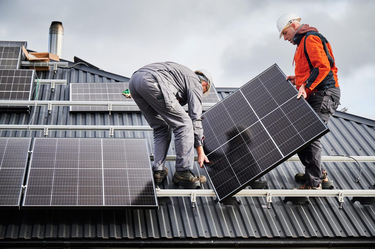 two workers installing solar panels on the roof of a house