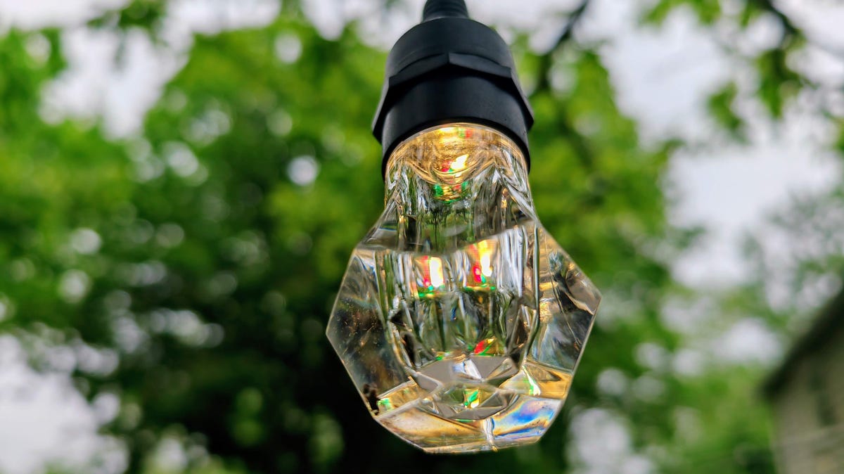 Close up of a single Nanoleaf String Light bulb during daylight with trees in background
