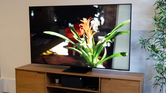 The Samsung QN90B QLED TV sits at an angle on a wooden tabletop stand.