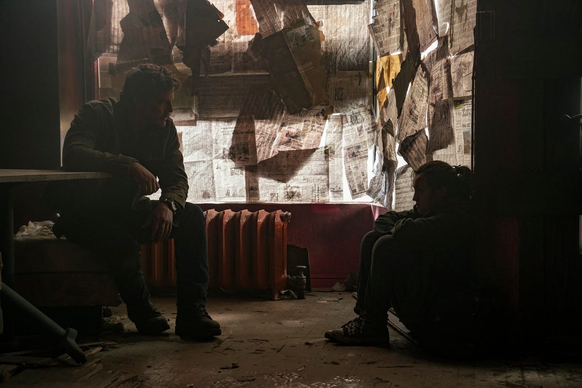 Joel and Ellie talk in an abandoned store with paper-covered windows in The Last of Us