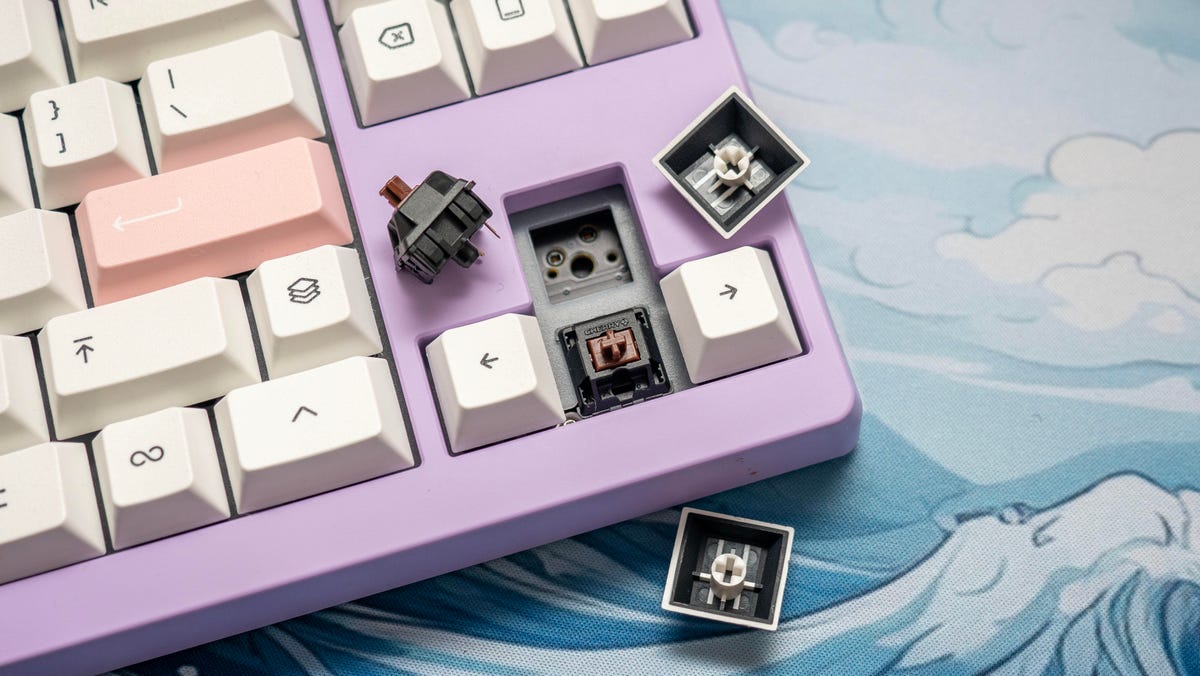 The right corner of the Monokei Standard mechanical keyboard in lilac with white keycaps with the up arrow keycap off and Cherry Brown keyswitch removed.