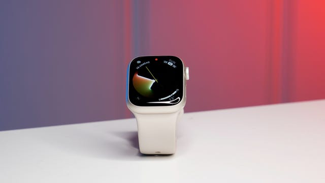 A white Apple Watch Series 7 on a white table against a red and blue background.