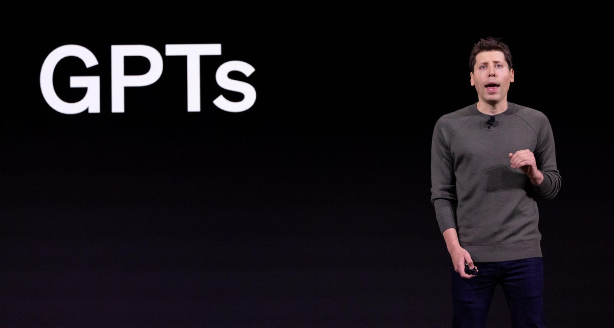 OpenAI CEO Sam Altman stands in front of a black screen that shows the term 