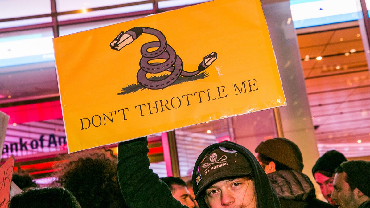 A protestor holds a yellow net neutrality sign that says "don't throttle me"