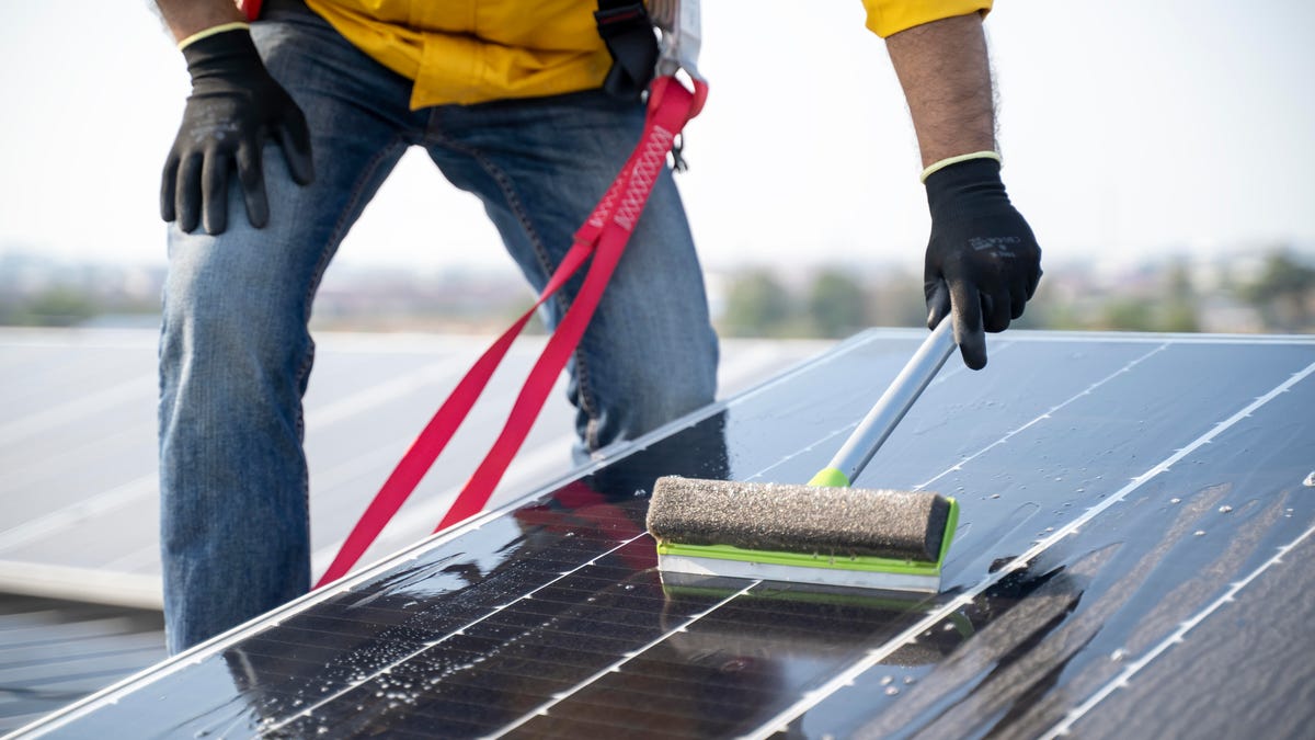 A man uses a squeegee to clean off a dusty solar panel.