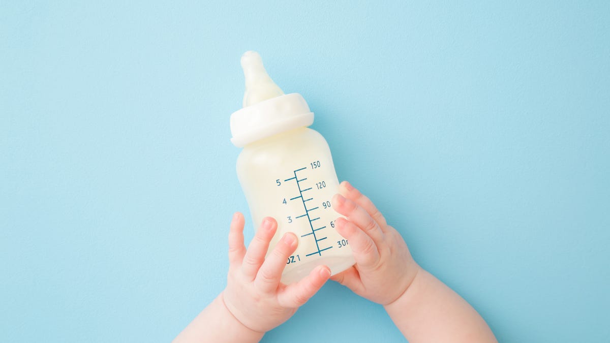 An infant holds a baby bottle