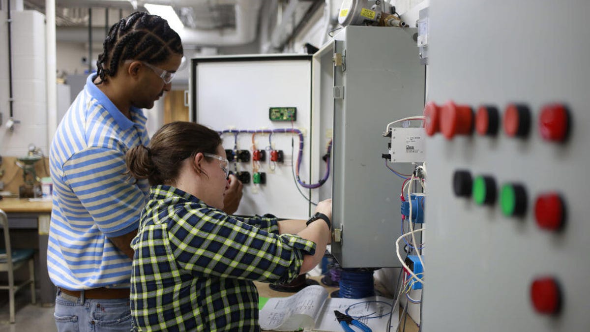 Two electrician apprentices work on a programmable logic controller.