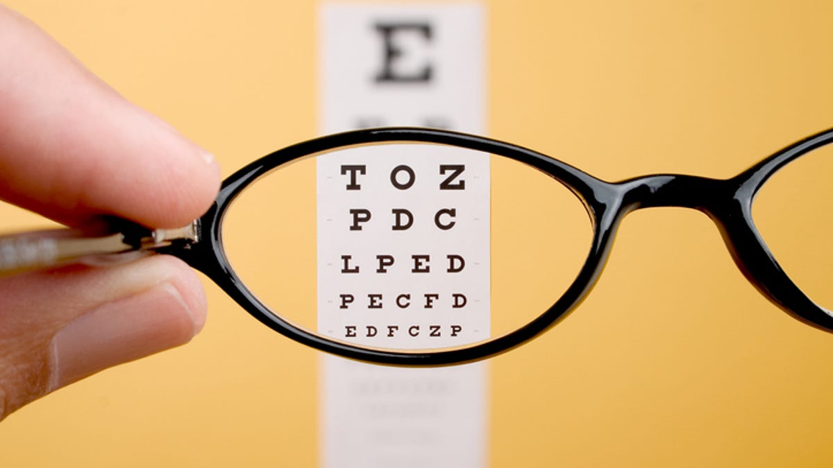 Pair of glasses being held in front of a Snellen Chart.