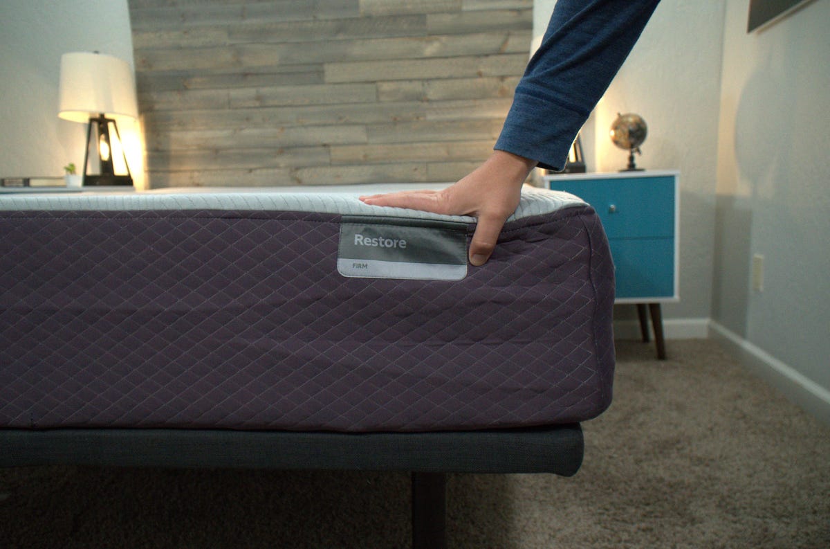 A closeup of the Purple Restore mattress and a person touching the cover.