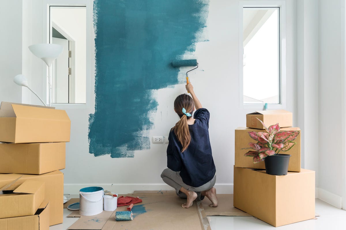 woman painting a wall green in a room with moving boxes