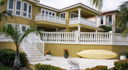 large yellow house with balconies and a patio surrounded by palm trees