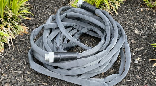 The Teknor Apex Zero-G Hose sits in a coil amidst some mulch.