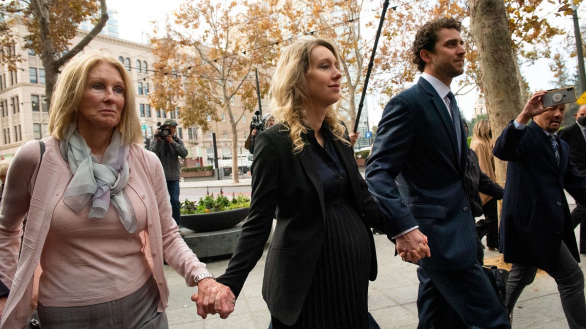 Theranos founder Elizabeth Holmes arrives at federal court in San Jose, California, wearing a black suit. Her mother, Noel Holmes, is on her left and partner Billy Evans is on her right
