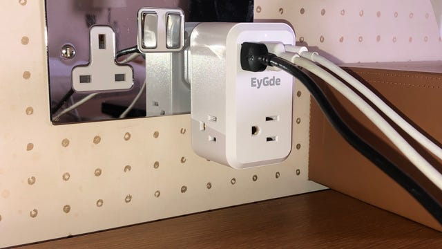 Three cables plugged into an adapter in an outlet above a desk