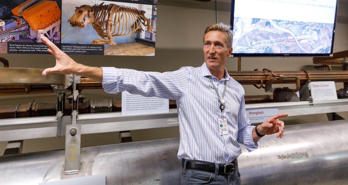 Mark Hogan​, scientific leader of a project called FACET-II to radically boost accelerator power, describes how SLAC's accelerator components work. The biggest pipe behind him is actually used just to house laser beams to ensure the accelerator components stay aligned correctly.