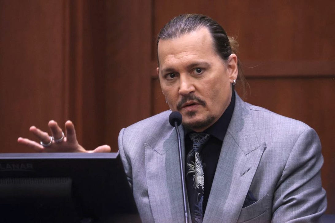 Johnny Depp on the stand during the trial. As he talks, he holds out his right hand, with fingers spread, as if emphasizing a point.