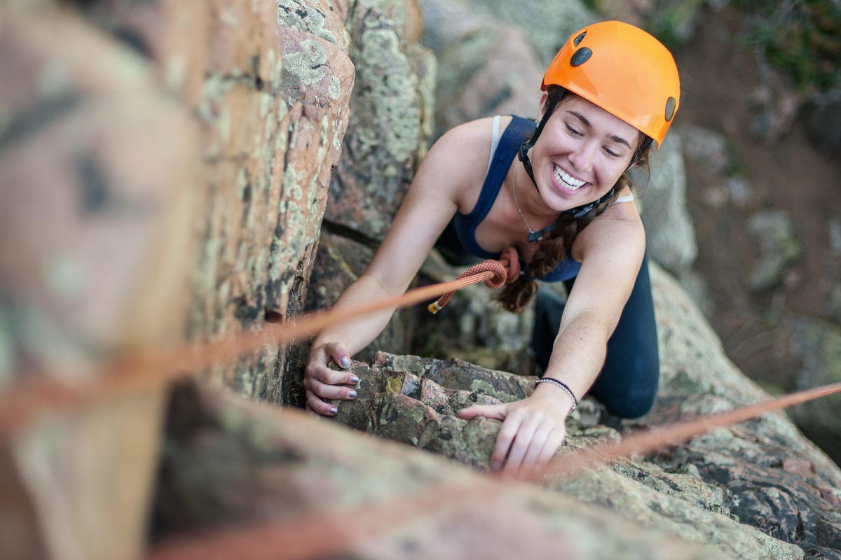 a young woman looks up and smiles as she ascends a rock climbing route