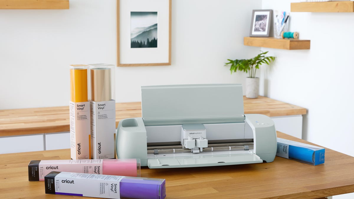 The Cricut Explore 3 vinyl cutting machine on a table with multiple different colored rolls of vinyl.