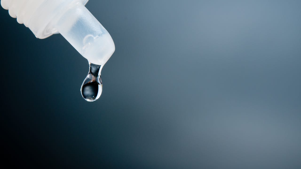 A close-up shot of an eye drop dripping out of a bottle